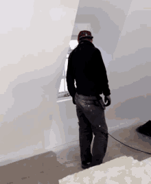 a man in a black jacket is standing in a room with a window