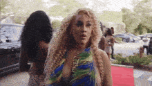 a woman with curly blonde hair is standing on a red carpet .