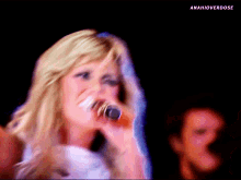 a blonde woman singing into a microphone with anahioverdose written on the bottom right