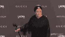 a woman with a cane stands in front of a wall that says gucci and lacma