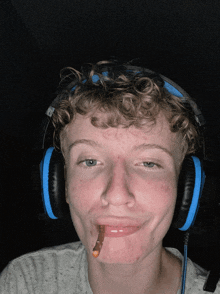 a young man wearing headphones holds a worm in his mouth