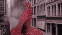 a man in a spiderman costume is covering his face with his hand while standing in front of a city street .