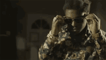 a man in a floral shirt and sunglasses is making a peace sign .