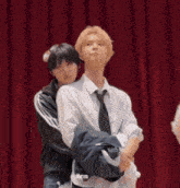 a man in a tie is hugging another man in front of a red curtain