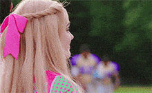 a woman with blonde hair and a pink bow in her hair is standing on a field .