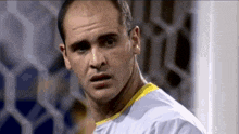 a man in a white shirt with a yellow stripe on the collar is standing in front of a soccer goal .