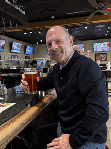 a bald man sitting at a bar holding a glass of beer