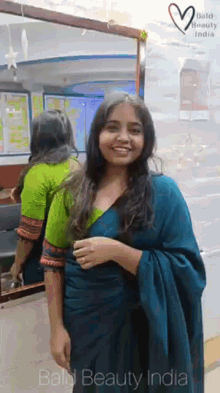 a woman in a blue saree is standing in front of a mirror in a salon .