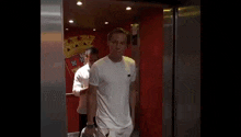 a man in a white t-shirt is walking into an elevator .