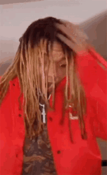 a man with dreadlocks is wearing a red jacket and holding his hair .