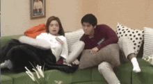 a man and a woman are sitting on a green couch with polka dot pillows .
