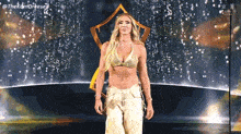 a woman in a gold bra and white pants is standing on a stage