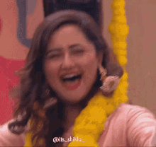 a woman wearing a pink shirt and a yellow garland around her neck laughs