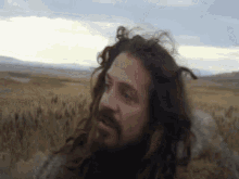 a man with long hair and a beard is in a field .