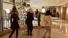 three women are dancing in front of a christmas tree in a hotel lobby