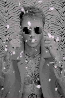 a black and white photo of a man wearing sunglasses and a coat with a tattoo on his chest that says sumo