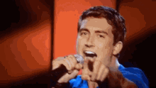 a man in a blue shirt is singing into a microphone on stage .