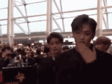 a man is covering his mouth with his hand in front of a crowd of people in an airport .