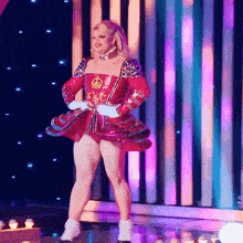a woman in a red dress is dancing on a stage with purple lights behind her
