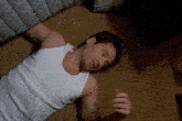 a man in a white tank top lays on the floor