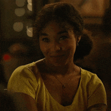 a woman wearing a yellow top and a necklace smiles