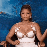 a woman in a white dress is sitting in a chair with her arms outstretched in front of an aquarium .