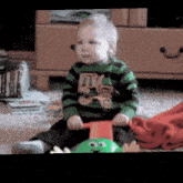 a baby in a green and black striped shirt is sitting on the floor playing with a toy