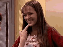 a woman in a red cardigan is smiling and touching her chin .
