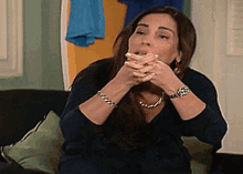 a woman is sitting on a couch covering her mouth with her hands .