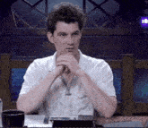 a man sits at a table with his hands folded
