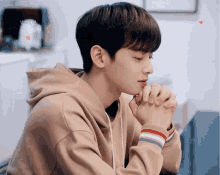 a young man in a tan hoodie with his hands folded in prayer