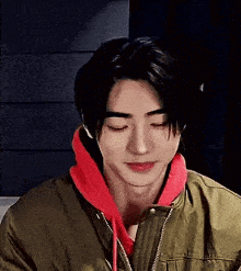 a young man wearing a green jacket and a red hoodie is smiling .