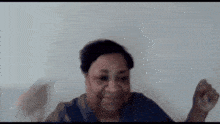 a woman in a blue shirt is making a funny face while standing in front of a white wall .