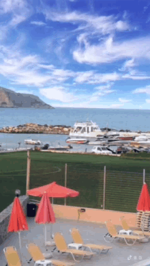 a swimming pool with red umbrellas and chairs in front of a body of water