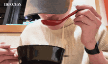 a person wearing a hat is eating from a bowl with a spoon and the word bigocean is visible in the corner