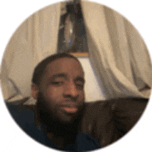 a man with a beard is sitting on a couch taking a selfie .