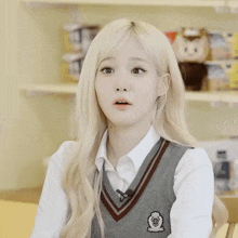 a girl with blonde hair wearing a white shirt and a gray vest with a badge on it