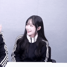 a girl wearing a black jacket with white stripes on the sleeves smiles for the camera