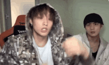 a man in a hoodie is standing next to another man in a room .