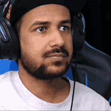 a man with a beard is wearing headphones and a baseball cap .
