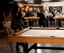a woman is standing next to a pool table with a pool cue