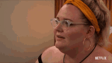 a woman wearing glasses and hoop earrings has a netflix logo behind her