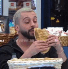a man with a beard is eating a sandwich in front of a sign that says www.bewin.com