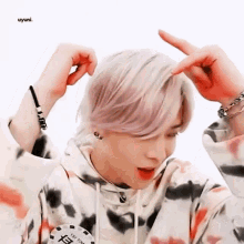 a young man with pink hair is making a heart shape with his hands .