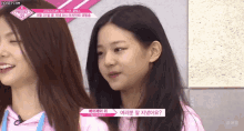 two girls are standing next to each other in front of a pink wall .