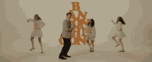 a man and two women are dancing in front of a stack of letters that say b and n