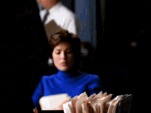 a woman in a blue sweater is sitting at a desk with papers