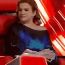 a woman in a blue dress is sitting in a red chair and looking at her phone .