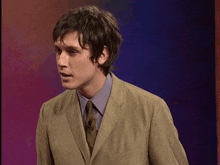 a man in a suit and tie stands in front of a purple backdrop