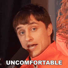 a man in an orange jacket is talking into a microphone and the word uncomfortable is visible on the bottom